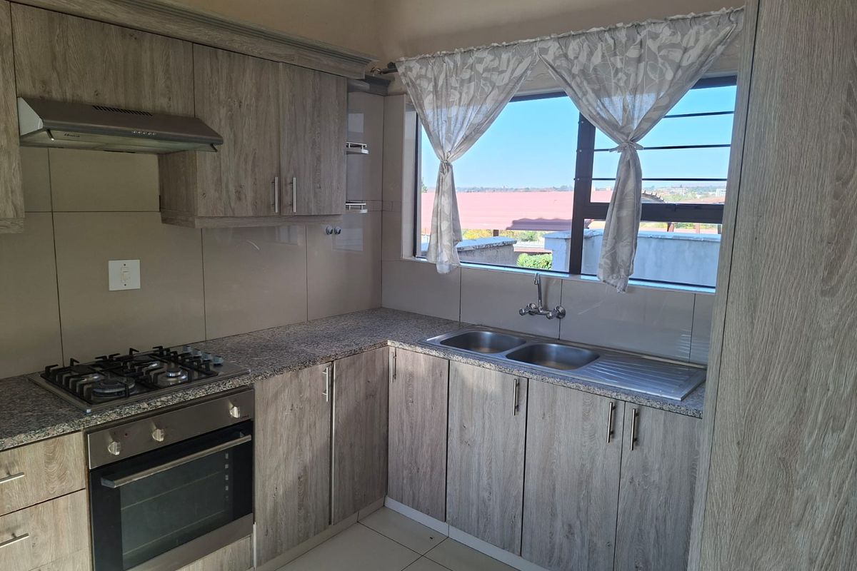 Modern kitchen featuring wood-grain cabinetry, granite countertops, a gas hob, built-in oven, and a double stainless steel sink with a window view.