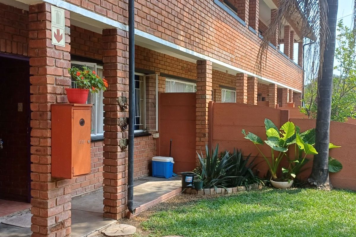 Ground floor apartment exterior featuring a brick facade, security gate, and a small private garden area with a concrete walkway.