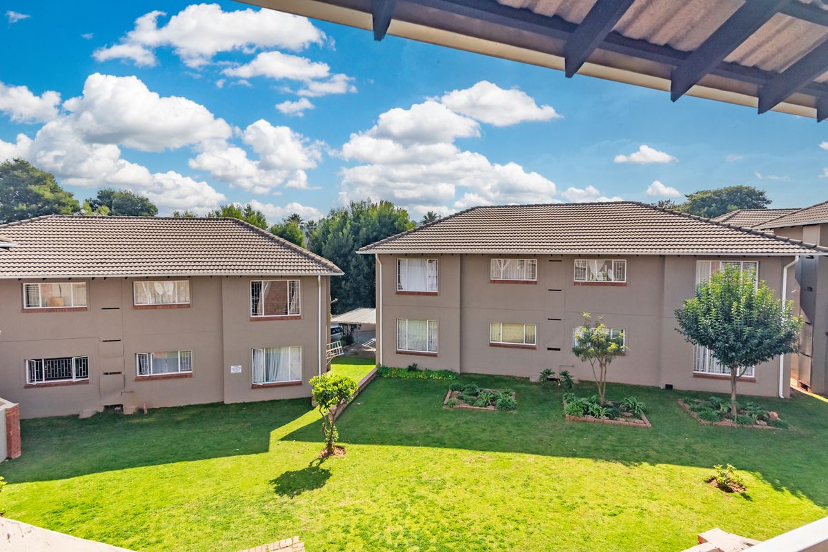 An elevated view of the rear exterior of the townhouse complex, featuring well-maintained communal gardens, tiled roofing, and established landscaping.