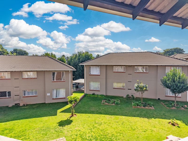 An elevated view of the rear exterior of the townhouse complex, featuring well-maintained communal gardens, tiled roofing, and established landscaping.