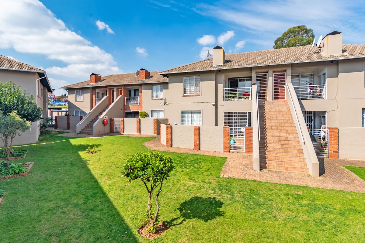 Rear view of a townhouse complex featuring multi-level units with external staircases, private balconies, and a shared landscaped garden area.
