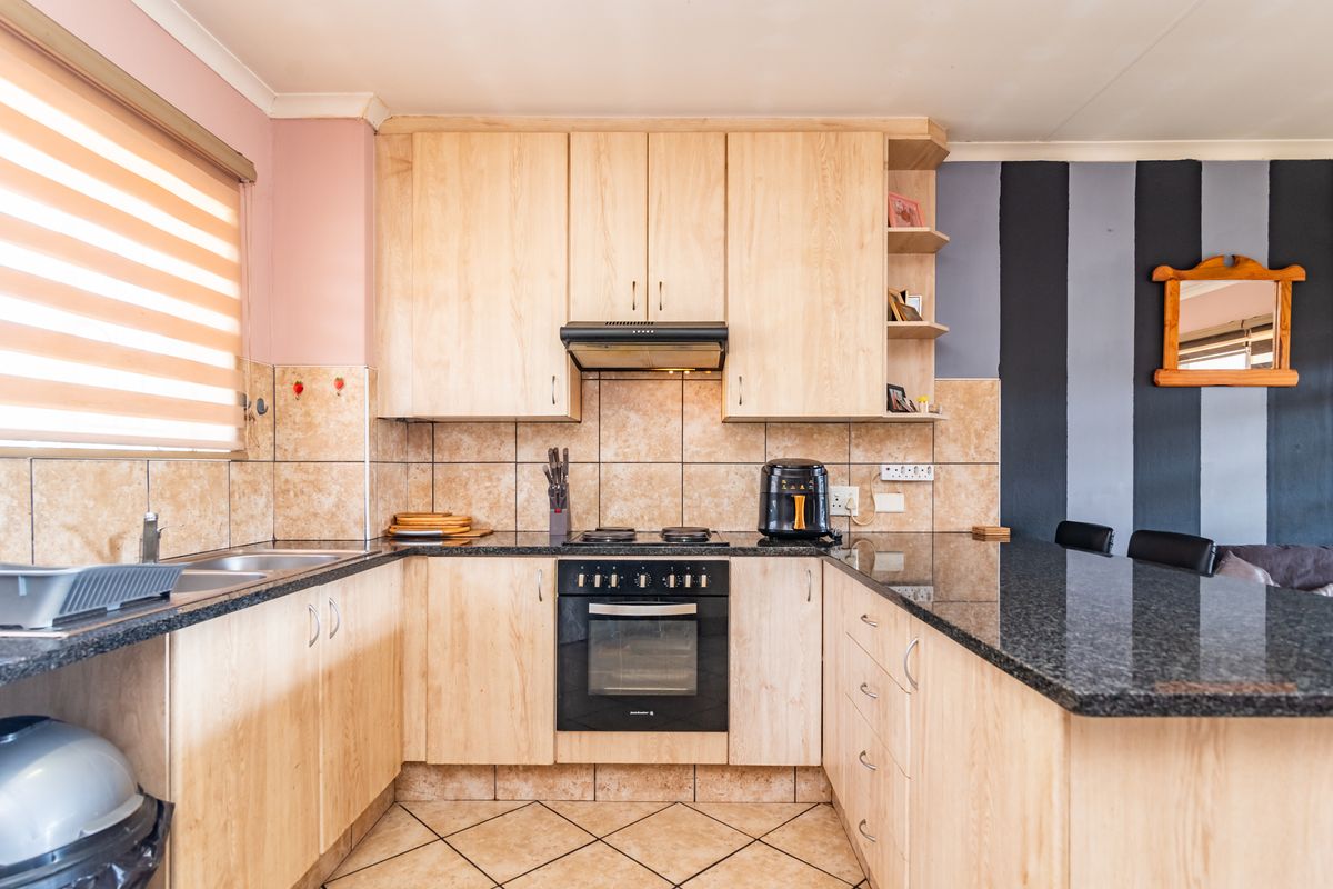 Functional kitchen featuring light wood cabinetry, granite countertops, built-in oven and hob, and a breakfast bar, with tiled backsplash and flooring.
