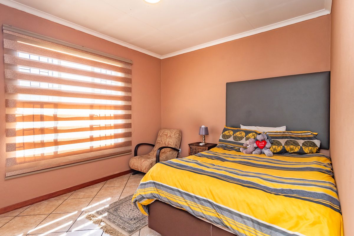 A bedroom featuring ceramic floor tiles, roller blinds, and security bars on the window, providing a functional and well-lit living space.