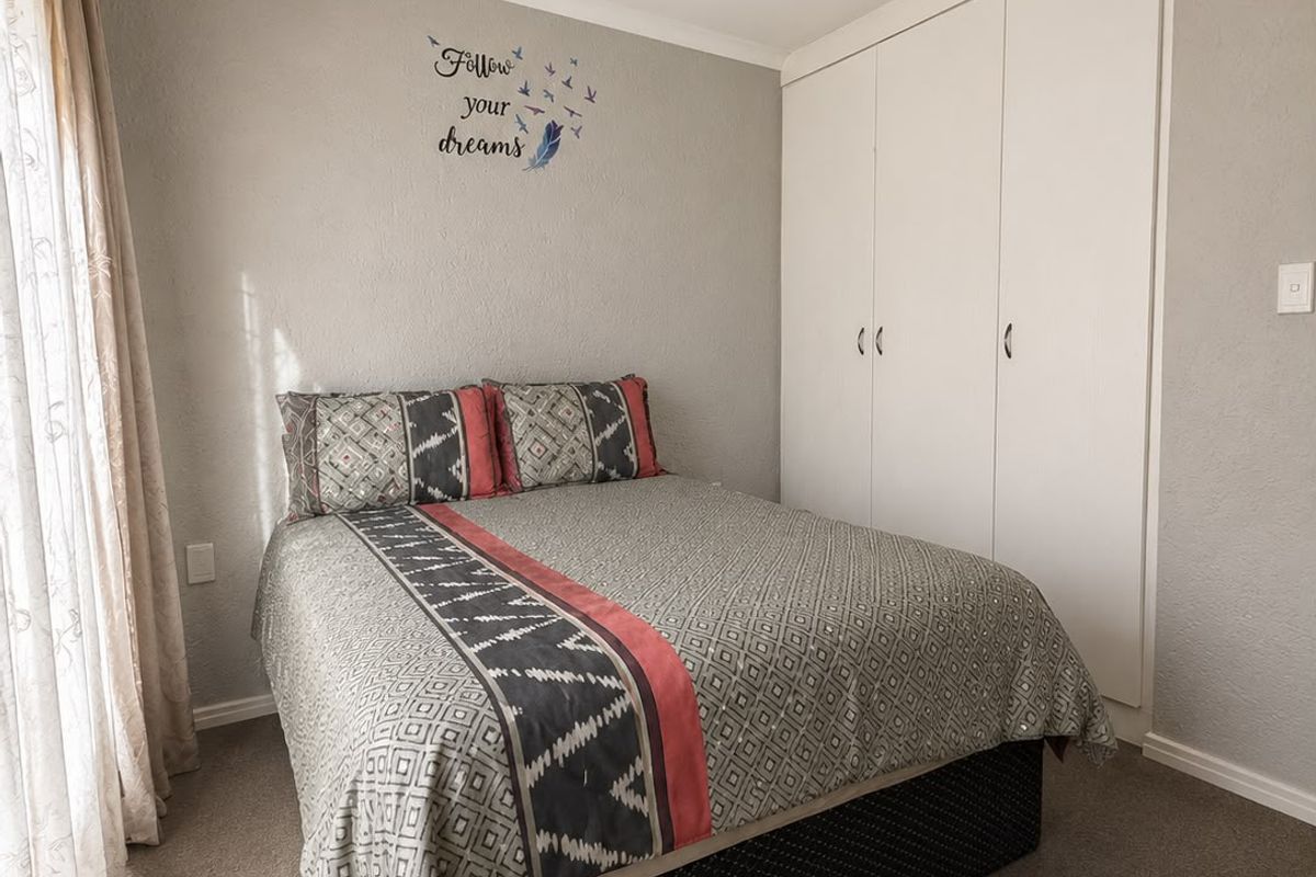 A functional bedroom featuring neutral wall tones, carpeted flooring, a ceiling fan, and built-in wardrobe storage.