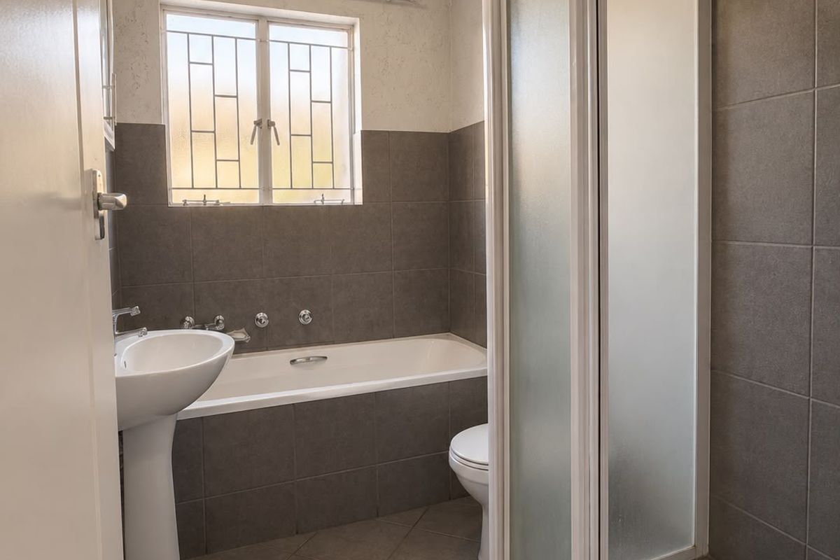 A functional bathroom featuring a pedestal basin, a built-in bathtub, and a separate shower enclosure with grey wall and floor tiling.