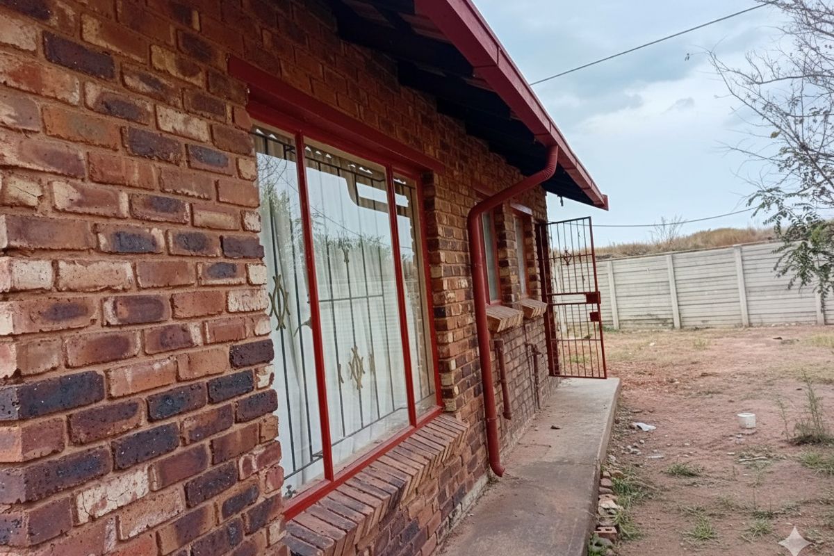Rear exterior view of a face brick house featuring metal security gates, concrete pathways, and a precast boundary wall.
