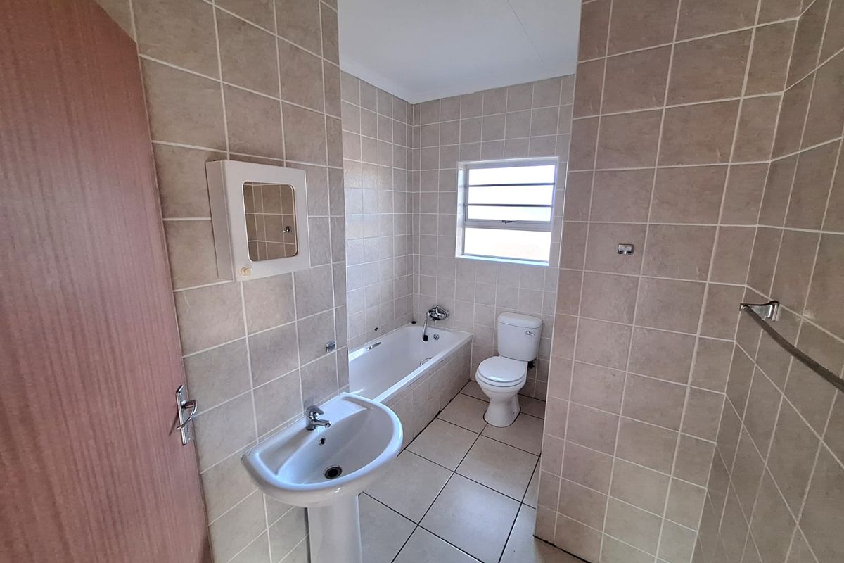 A functional bathroom featuring a pedestal sink, a standard bathtub, and a toilet, finished with neutral wall and floor tiling.