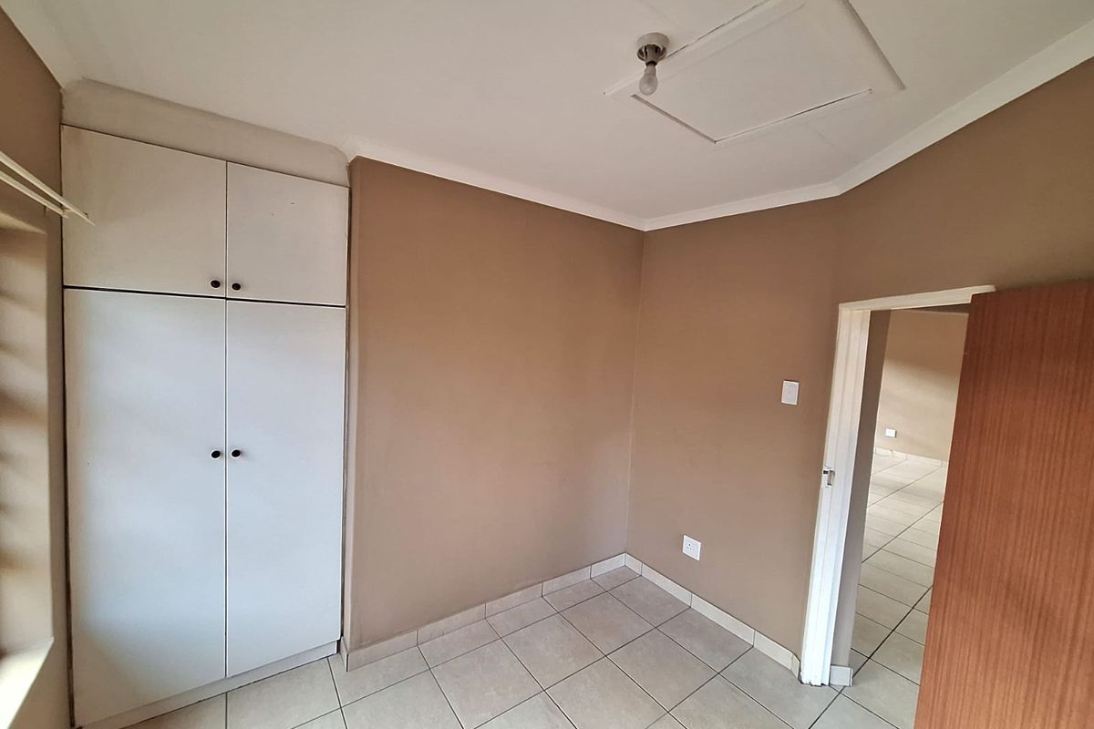 A compact bedroom featuring built-in white cabinetry, neutral wall tones, and tiled flooring, offering a clean and functional space.