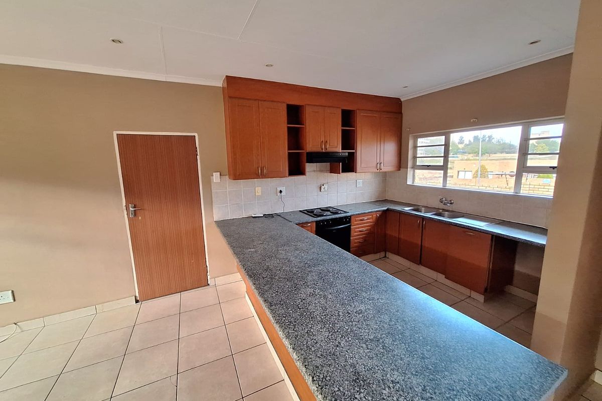 A functional kitchen featuring wooden cabinetry, a granite-look breakfast bar, built-in oven and hob, and tiled flooring.