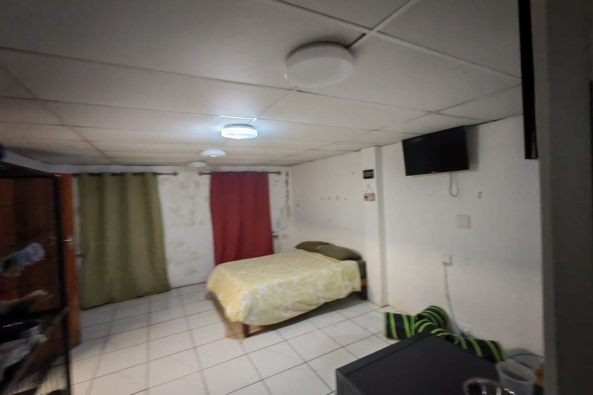 A bedroom featuring tiled flooring and a drop ceiling, currently showing significant signs of wear and wall damage.