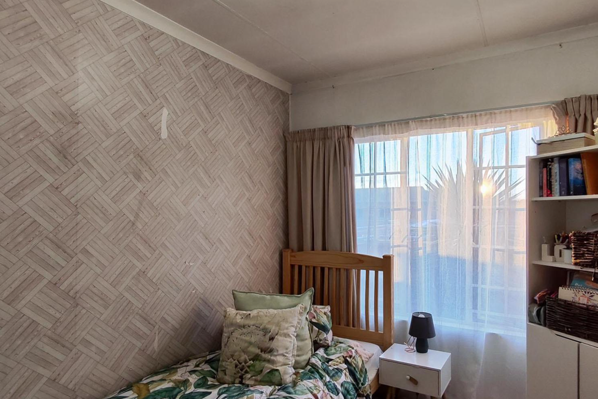 A bedroom featuring patterned wallpaper and a window with curtain tracks, showing signs of wear on the wall surface.