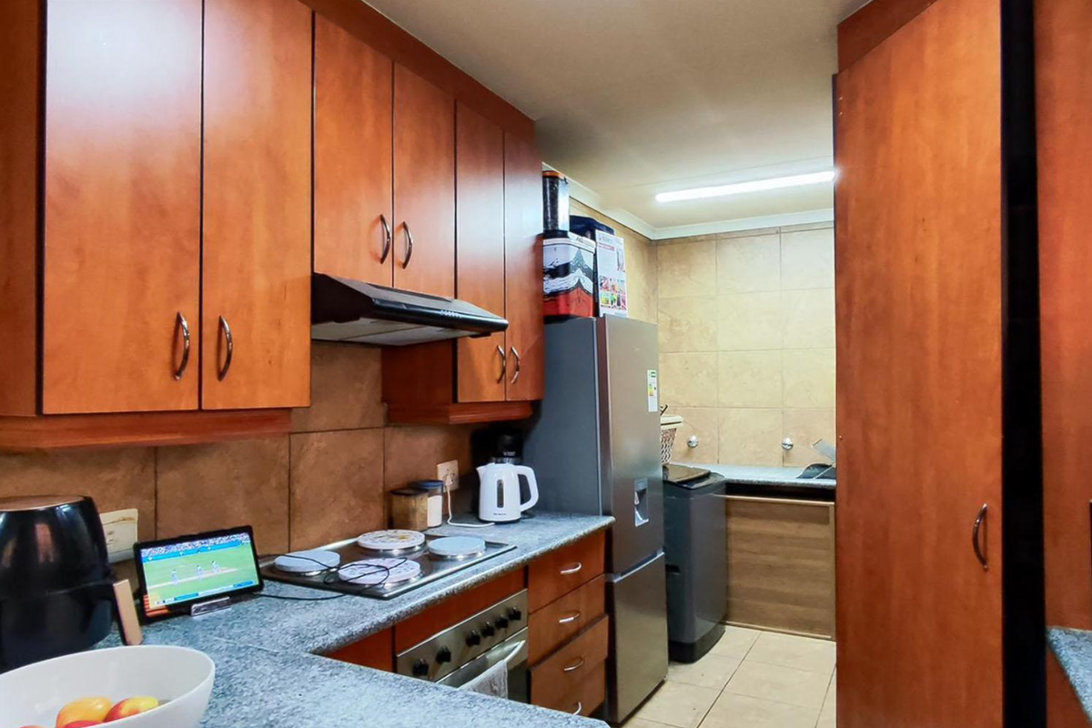 A functional kitchen featuring wood-finish cabinetry, stone-look countertops, built-in oven, electric hob, and tiled backsplash, with an adjacent utility area.
