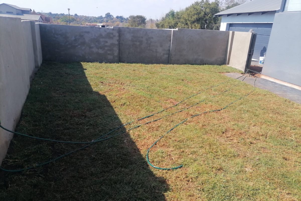 A private rear garden area featuring a lawn enclosed by high, unfinished concrete boundary walls, adjacent to the main dwelling structure.