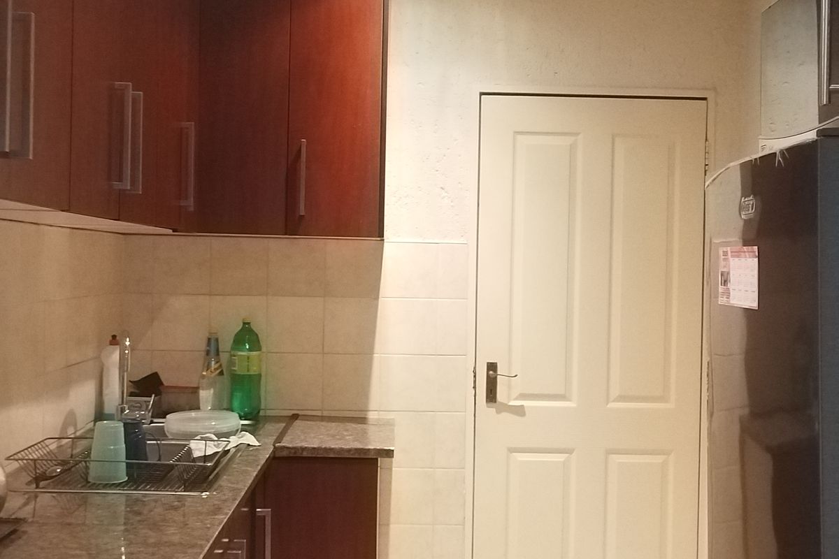 A functional kitchen featuring dark wood cabinetry, stone-look laminate countertops, tiled splashbacks, and tiled flooring.