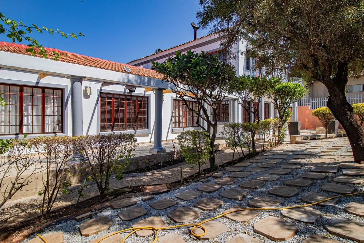 Rear exterior view featuring a covered patio with stone columns, terracotta roof tiles, and a landscaped garden with a paved stone walkway.