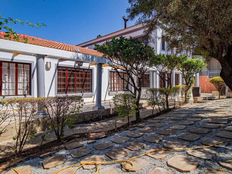 Rear exterior view featuring a covered patio with stone columns, terracotta roof tiles, and a landscaped garden with a paved stone walkway.