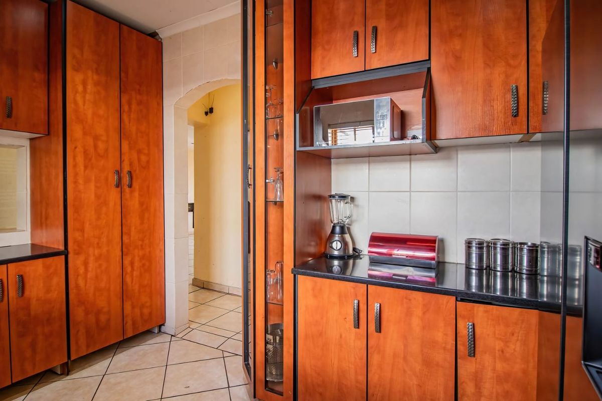 A functional kitchen featuring warm-toned wood cabinetry, dark laminate countertops, tiled backsplash, and tiled flooring with an arched doorway leading to adjacent rooms.