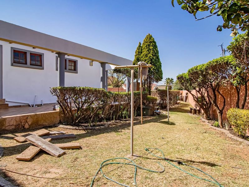 Rear exterior view featuring a covered patio with concrete columns, a tiled floor, and a garden area with boundary walls.