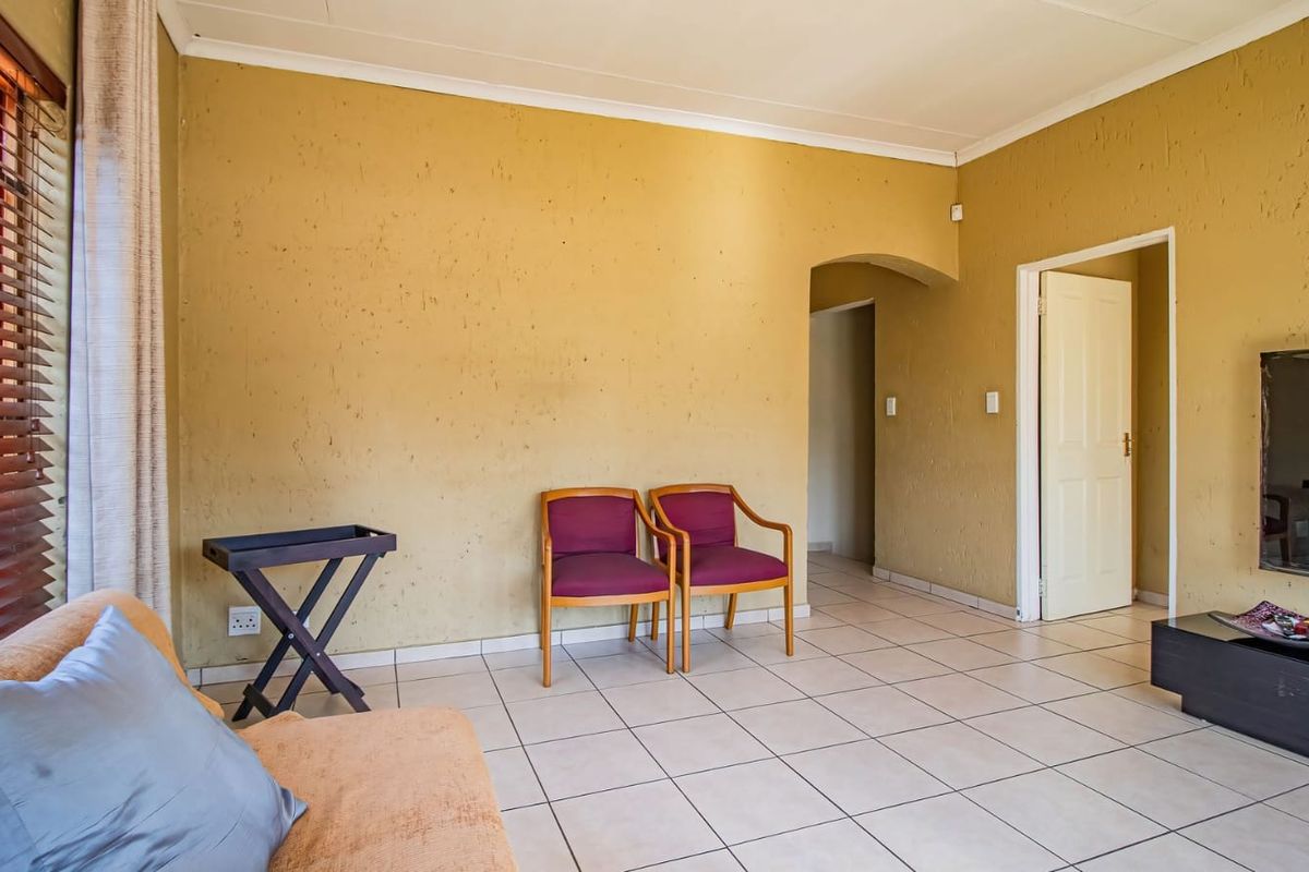A living room featuring tiled flooring, textured walls, and an arched doorway leading to an adjacent space, complemented by wooden window blinds.