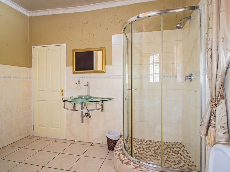 Bathroom featuring a curved glass shower enclosure, glass vessel sink, and tiled finishes. The walls require maintenance and repainting.