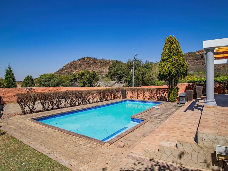 Outdoor pool area featuring a swimming pool, tiled patio, and stone-clad retaining wall with mountain views.