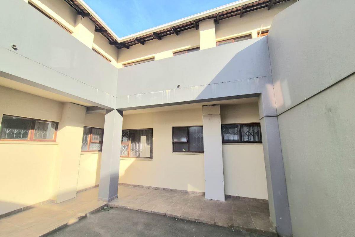 A rear exterior view of the apartment building featuring a covered tiled patio area, security-fitted windows, and concrete structural pillars.