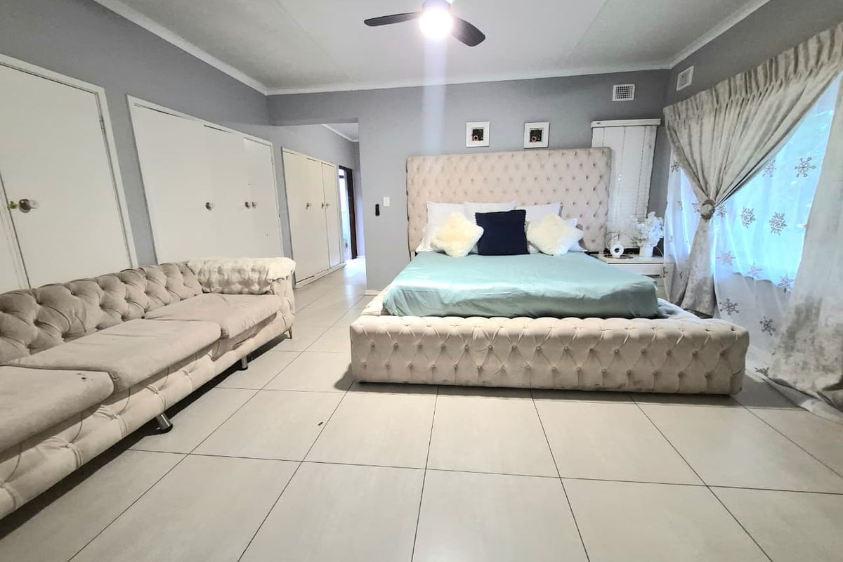 Spacious bedroom featuring neutral tiled flooring, built-in cupboards, and a central ceiling fan, offering a comfortable and functional living space.