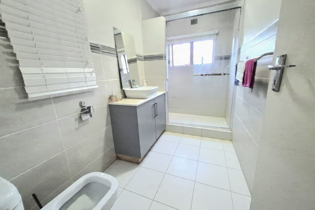 A clean, modern bathroom featuring a vanity with a vessel sink, a walk-in shower enclosure, and neutral floor-to-ceiling wall tiles.