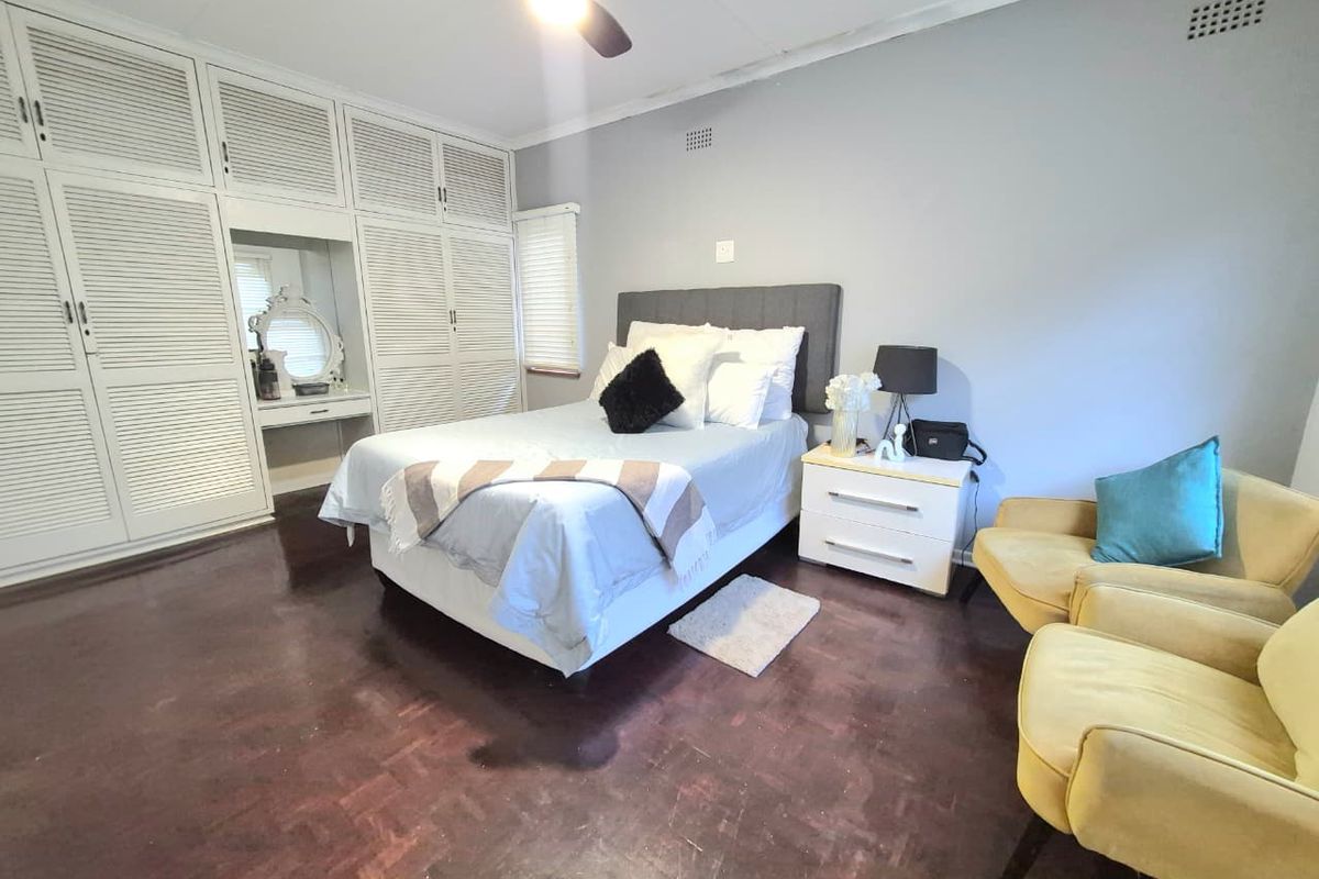 Spacious bedroom featuring extensive built-in cupboards with integrated vanity, ceiling fan, and traditional parquet flooring.