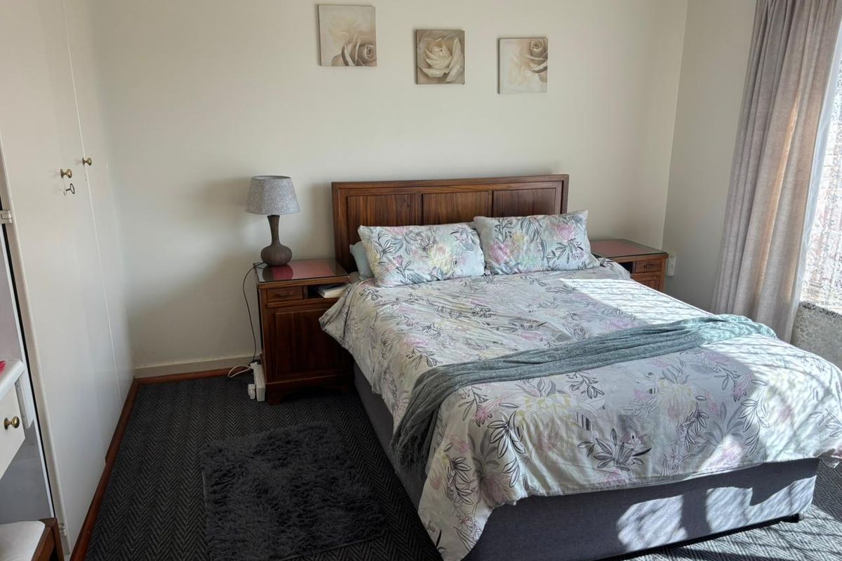 A functional bedroom featuring neutral walls, patterned carpeting, and a built-in wardrobe, offering a comfortable and well-maintained living space.