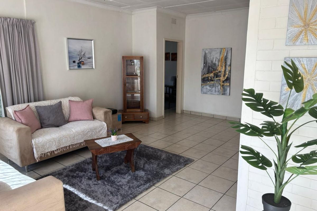 A spacious living area featuring neutral tiled flooring, a textured brick feature wall, and a classic tiled ceiling.
