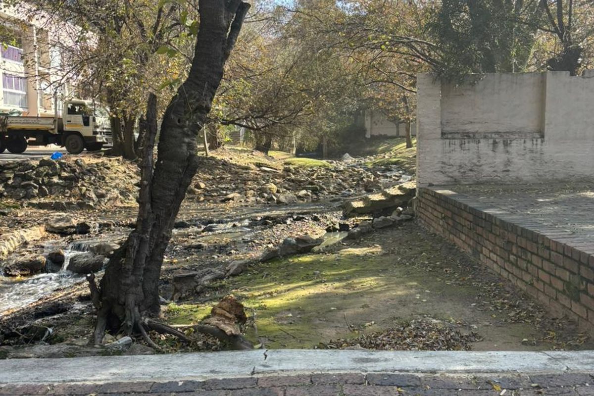 A view of the rear outdoor area featuring brick paving, a retaining wall, and a natural stream running through the property grounds.