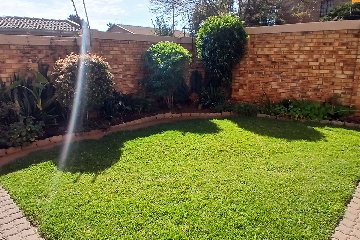 A private rear garden featuring a well-maintained lawn, established perimeter brick walling, and paved pathways.