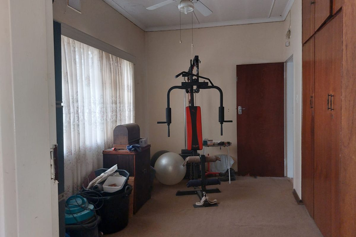 A bedroom featuring built-in wooden cupboards, carpeted flooring, and a ceiling fan, currently utilized as a home gym space.