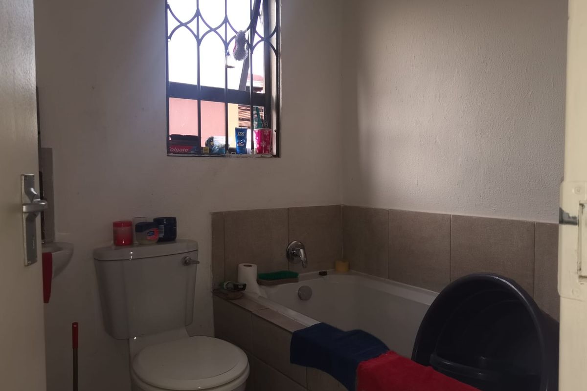 A functional bathroom featuring a bathtub, toilet, and basin with tiled splashbacks and security bars on the window.