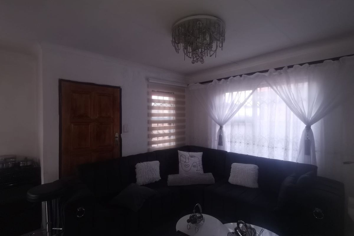 A living room featuring a crystal chandelier, timber door, and window treatments including roller blinds and sheer curtains.
