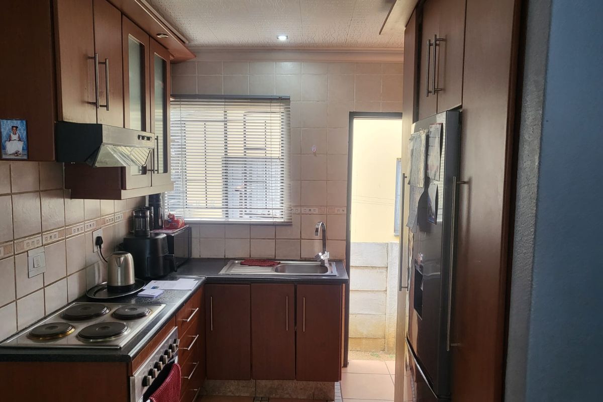 A functional kitchen featuring wood-finish cabinetry, tiled backsplash, integrated electric hob and oven, and direct access to an outdoor area.