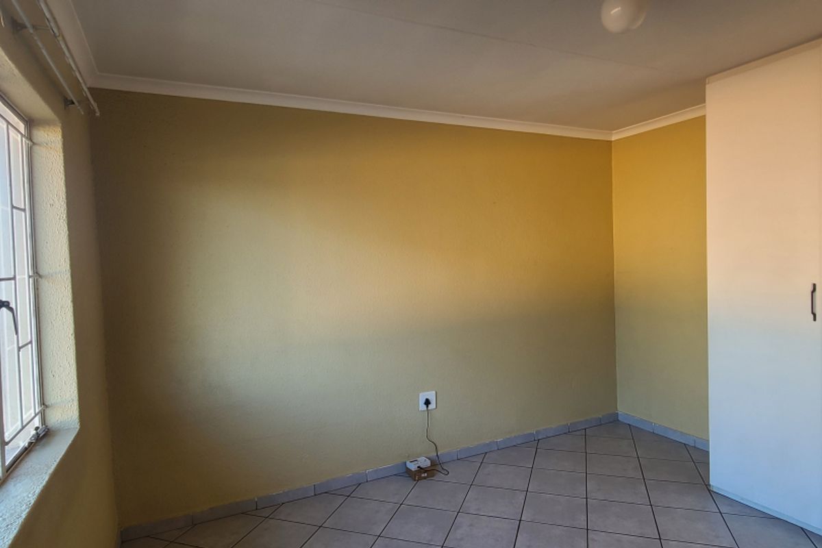 An empty bedroom featuring tiled flooring, a built-in wardrobe, and large windows with security bars, offering a blank canvas for personalization.