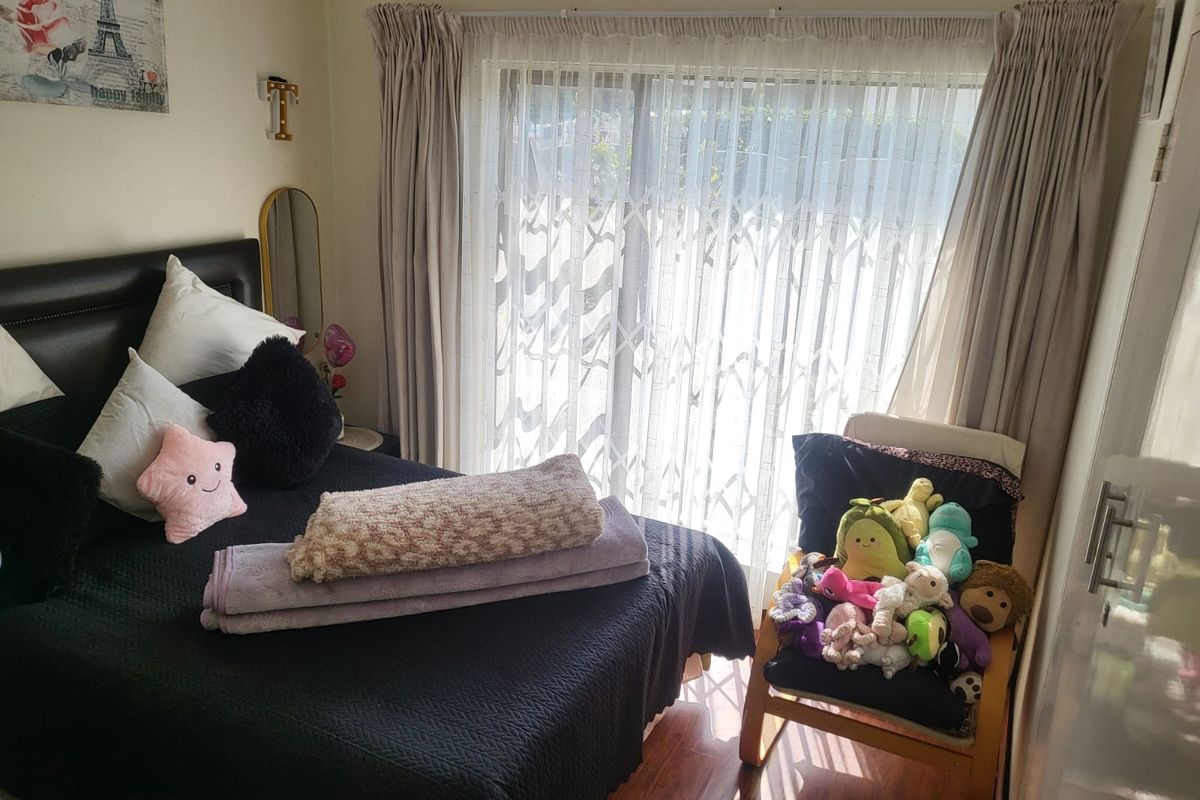 A bedroom featuring laminate flooring and a sliding glass door with security gate, providing access to the exterior.