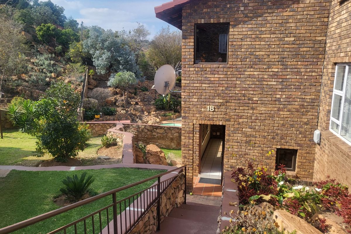 Rear view of a face brick townhouse featuring a paved walkway, metal railings, and a landscaped garden area with stone retaining walls.
