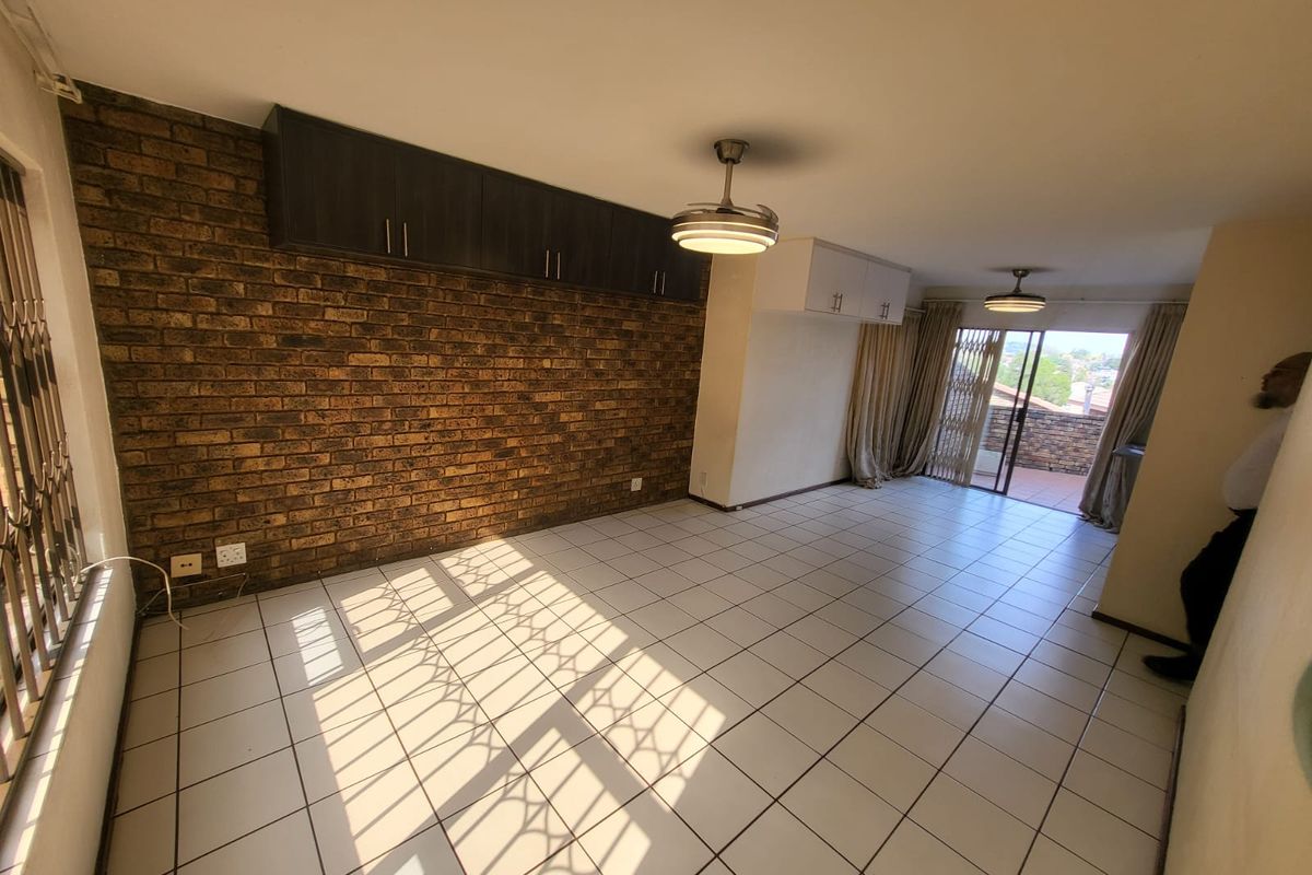 Spacious living area featuring an exposed brick wall, built-in overhead storage, tiled flooring, and direct access to an outdoor balcony.