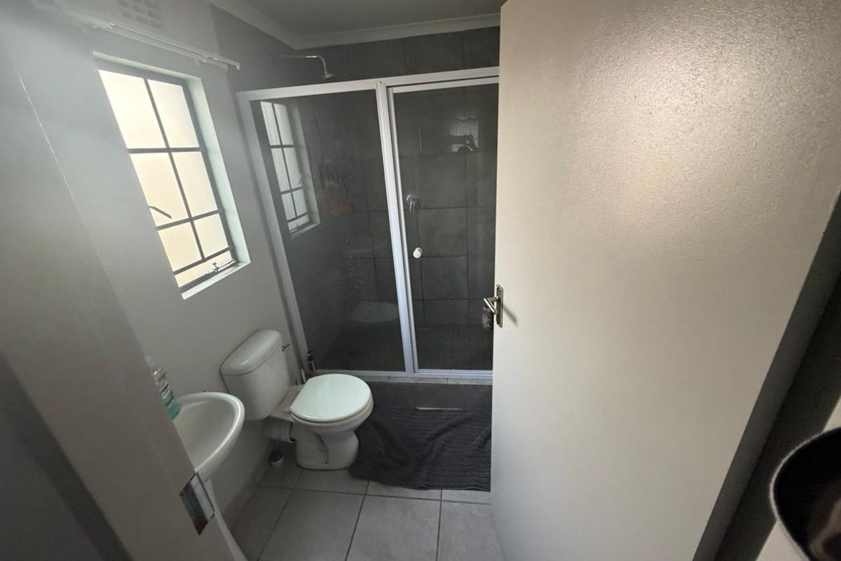 A functional bathroom featuring a glass-enclosed shower, pedestal basin, and toilet with tiled flooring and walls.