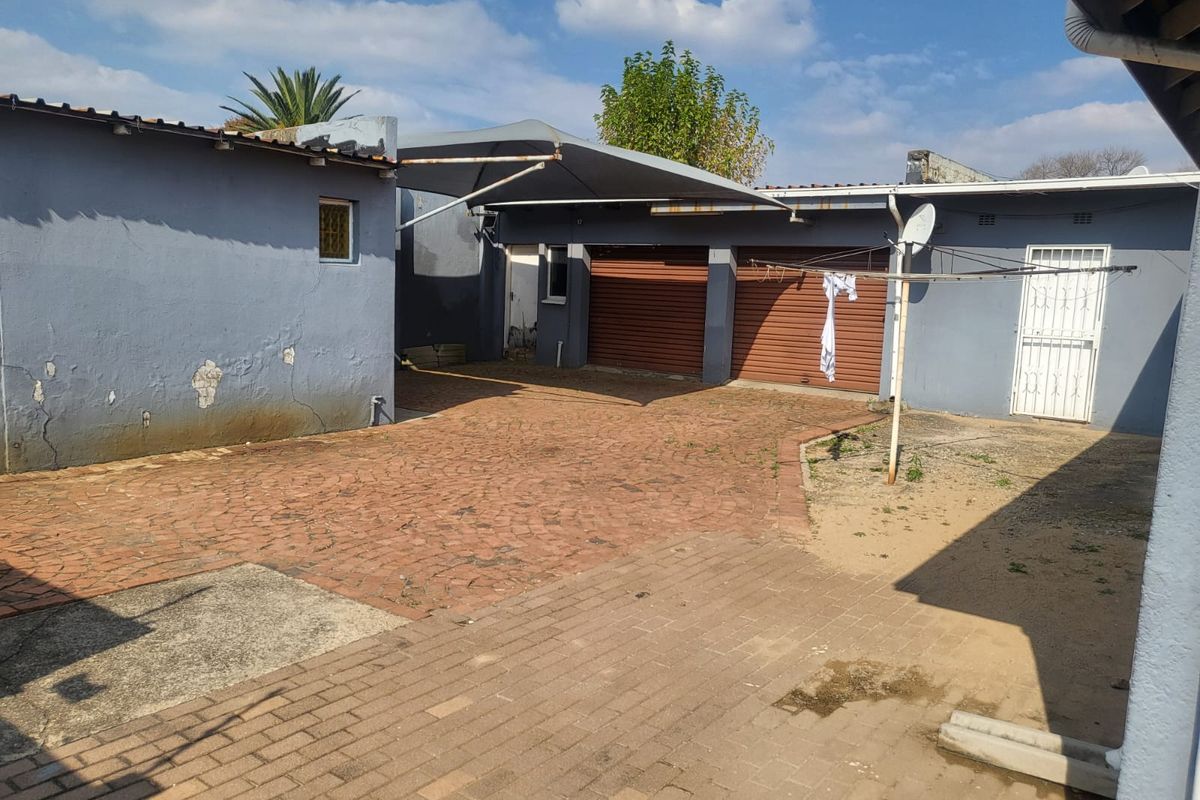 Rear exterior view featuring a paved driveway, double garage with roll-up doors, and a shade sail structure.