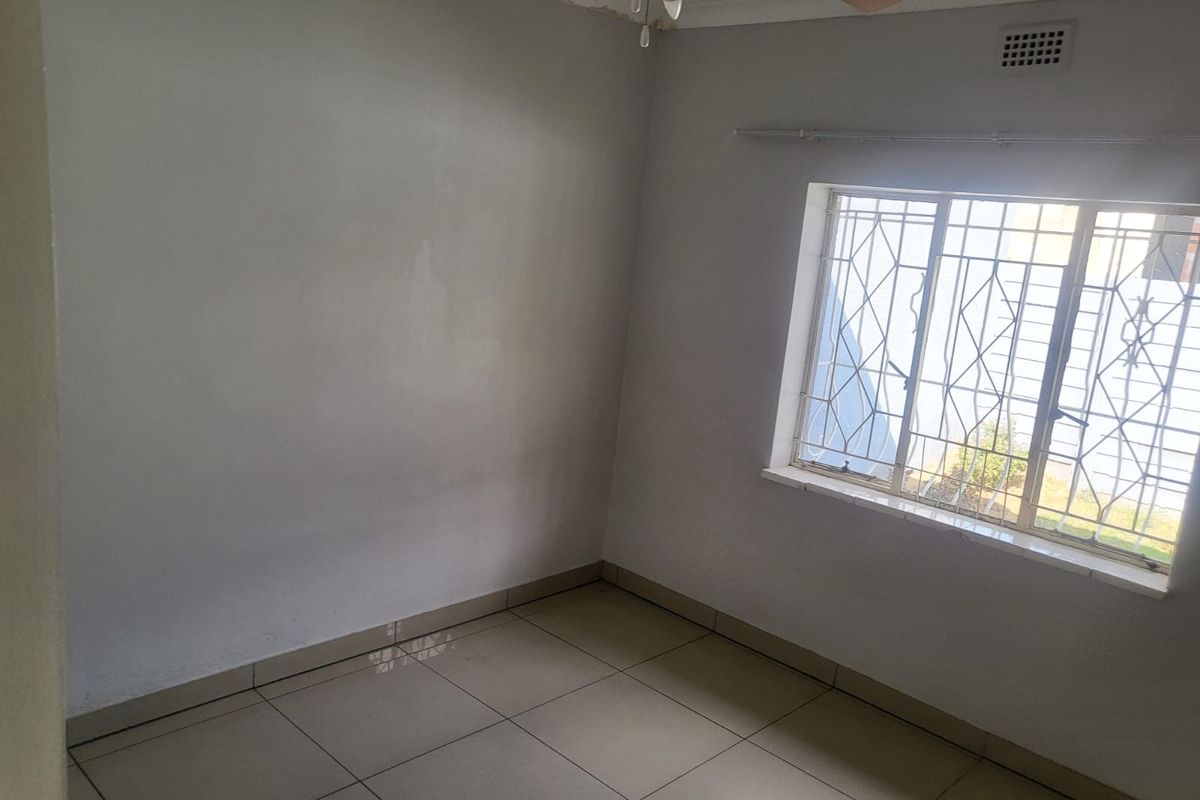 An empty bedroom featuring tiled flooring, a ceiling fan, and security bars on the window. The room requires minor cosmetic updates.