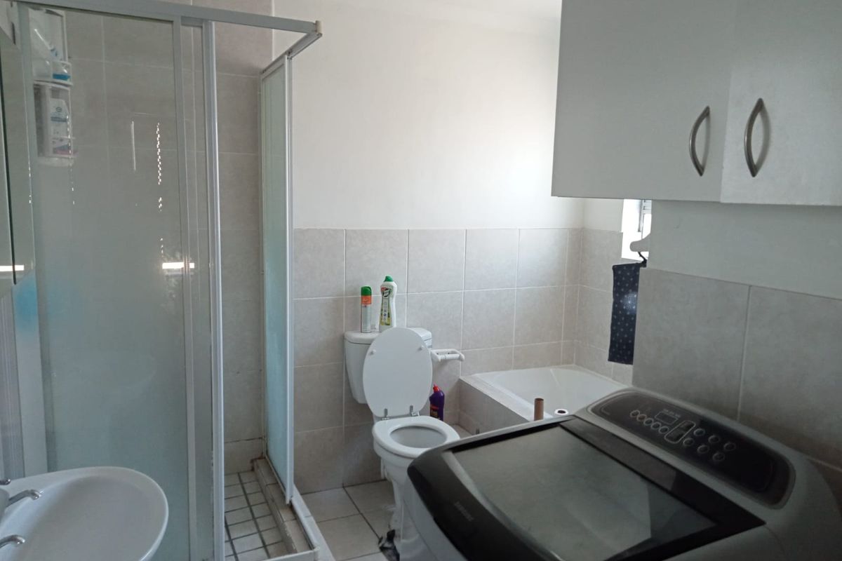 A functional bathroom featuring a glass-enclosed shower, a built-in bathtub, a toilet, and a wall-mounted vanity cabinet with integrated laundry space.