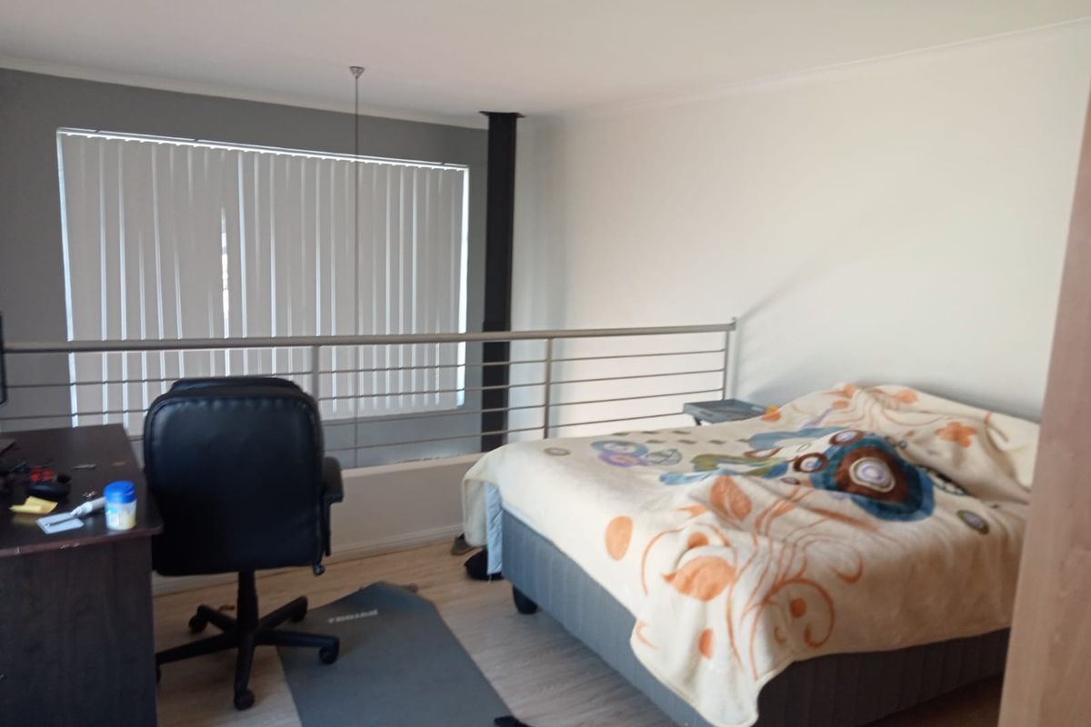 A loft-style bedroom featuring laminate flooring, a metal safety railing overlooking the lower level, and vertical window blinds.