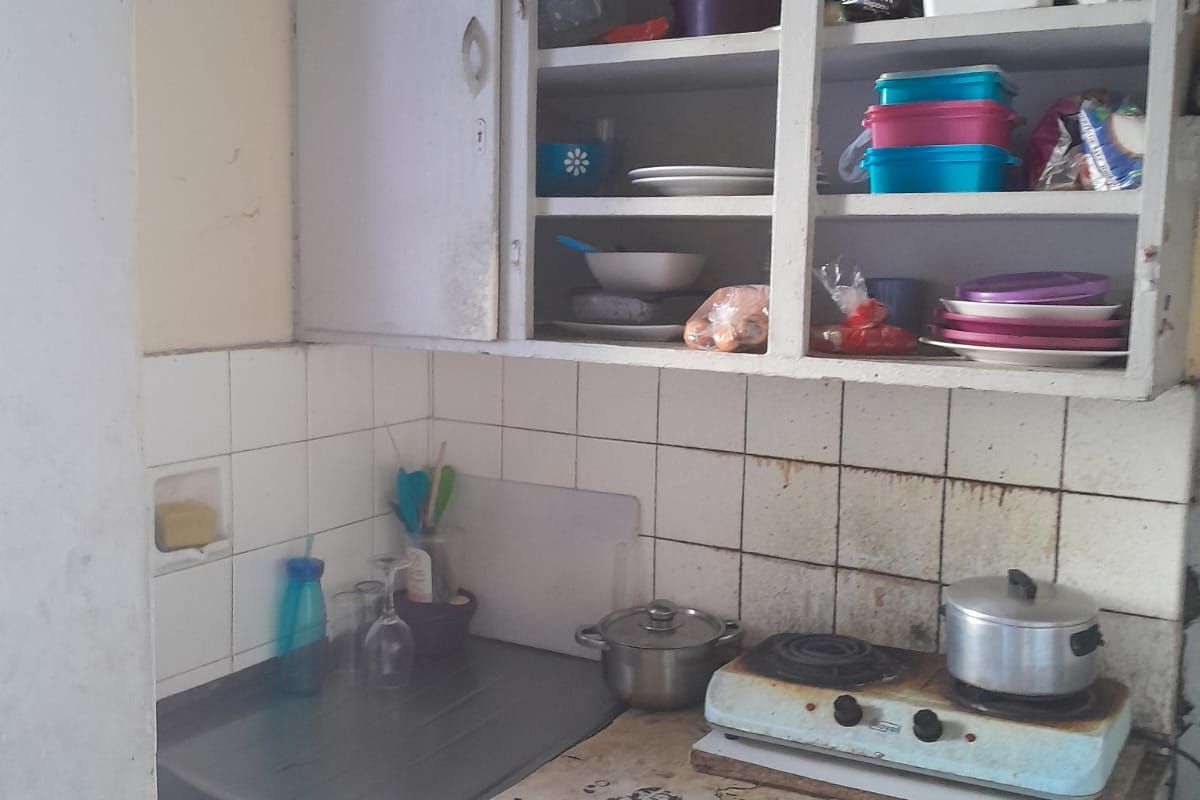 A compact kitchen area featuring built-in cabinetry, a stainless steel sink, and tiled splashbacks, currently showing significant signs of wear and dated finishes.