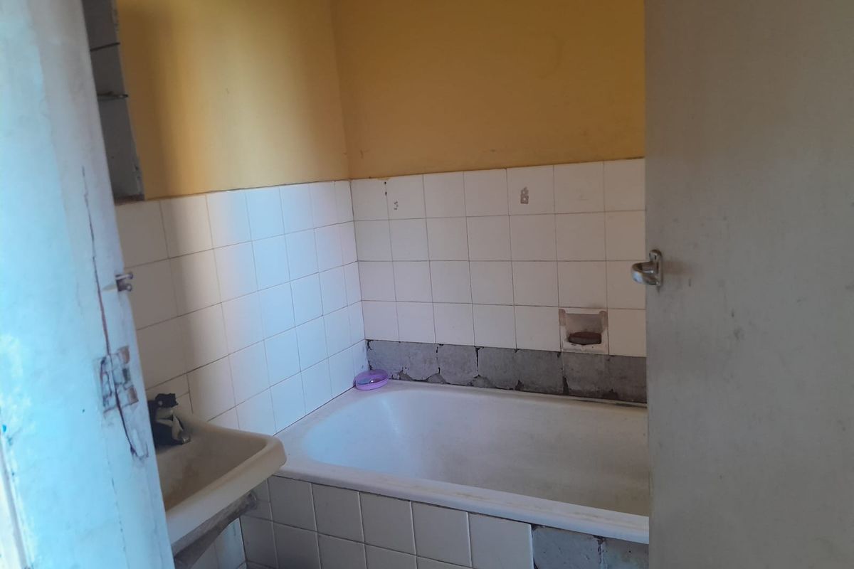 A dated bathroom featuring a bathtub and wall-mounted basin, currently requiring significant repairs to wall tiling and finishes.