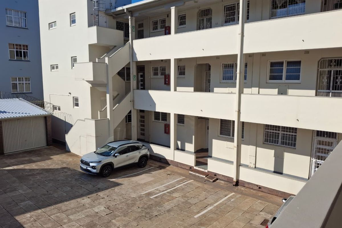 Exterior view of the apartment building complex featuring a paved courtyard, designated parking bays, and external stairwell access to upper levels.