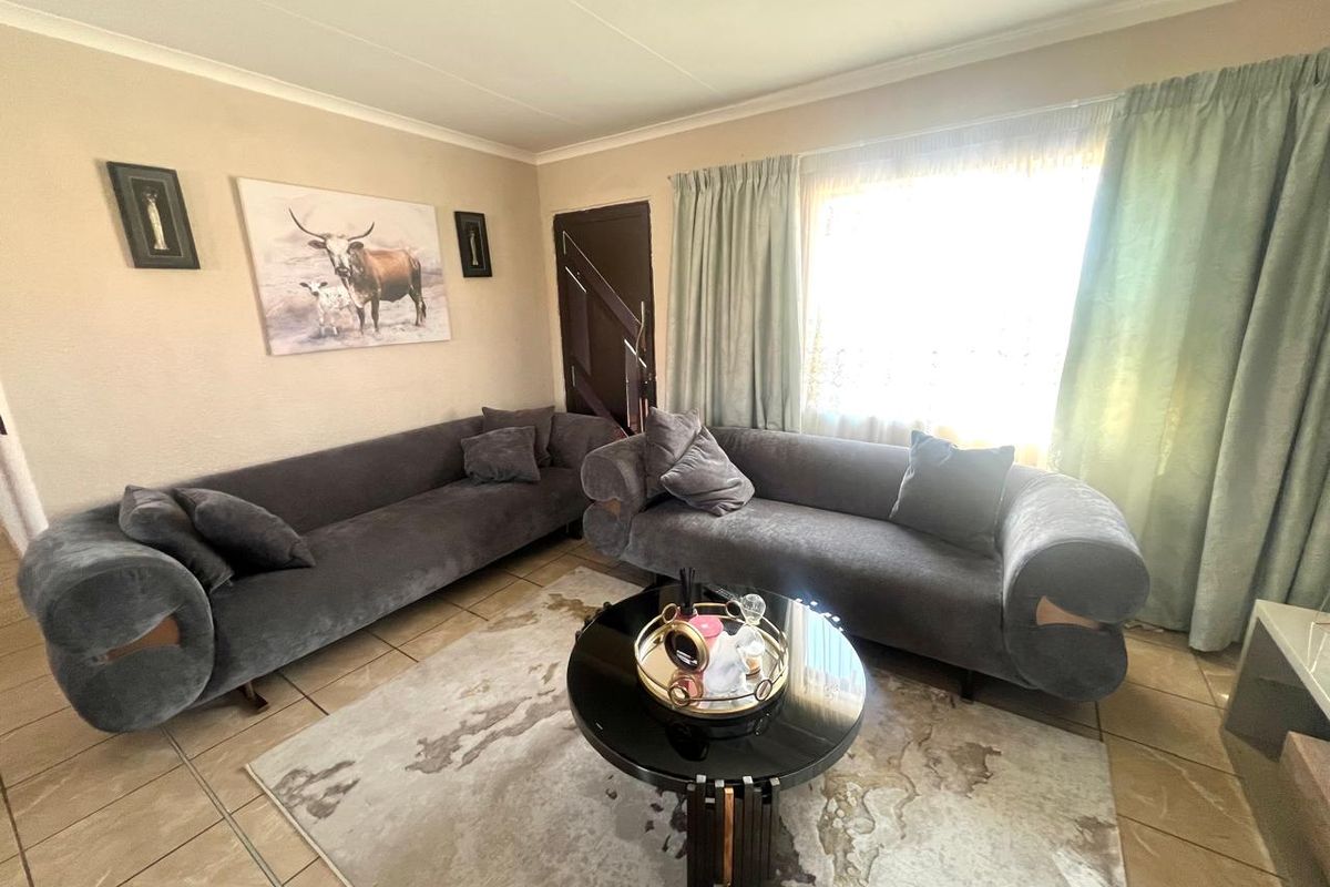 A comfortable living room featuring tiled flooring, coved ceilings, and natural light through a large window with curtain treatments.